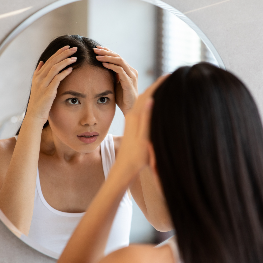 Woman looking worried at her hair in a mirror because she wants to stop hair loss and grow hair fast