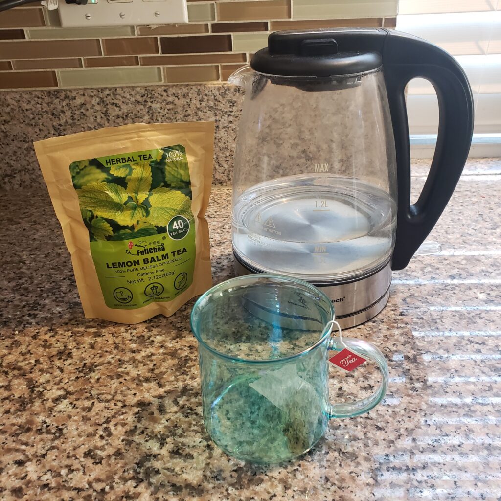 lemon balm tea, water cooker and cup with a tea bag in it.